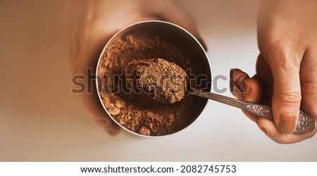 Top view of a jar with fragrant natural cocoa powder, which the woman takes out of the jar with a beautiful silver teaspoon. The process of making a delicious drink for breakfast.