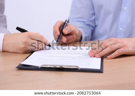 Businesspeople signing contract at wooden table, closeup of hands