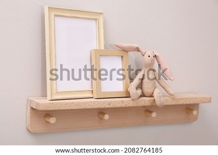 Wooden shelf with toy bunny and photo frames on beige wall. Interior element