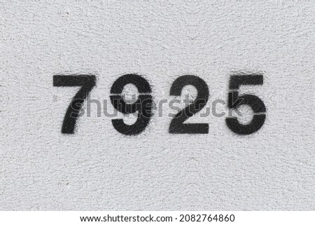 Black Number 7925 on the white wall. Spray paint. Number seven thousand nine hundred and twenty five.
