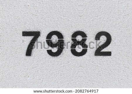 Black Number 7982 on the white wall. Spray paint. Number seven thousand nine hundred and eighty two.