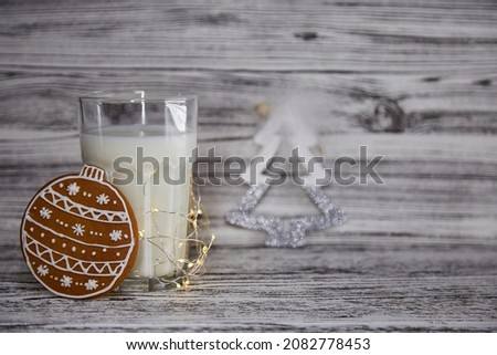 Milk with cookie for Santa concept. Handmade fresh cookies and glass with milk on the vintage wooden table. Cute Christmas tradition. Festive Christmas mood with garlands background. Copy space,
