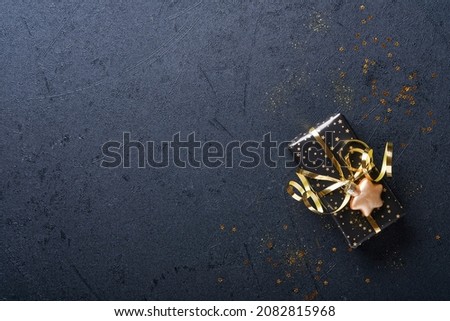 Holiday gift box or present with ribbon, golden confetti and gold baubles on black background. Magic christmas greeting card. Christmas Decoration. Border design. Mock up. Top view.