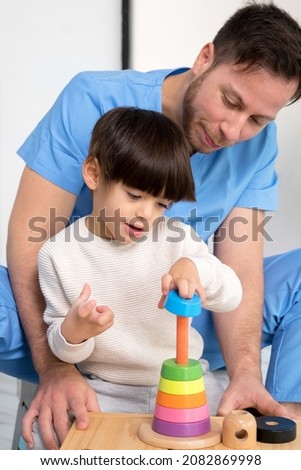 Young therapist helping cute little boy who has cerebral palsy, playing with developing toy at rehabilitation clinic. High quality photo Royalty-Free Stock Photo #2082869998