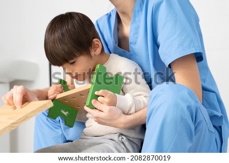 cute kid with disability playing with developing toys while is being helped by physiotherapist in rehabilitation hospital. High quality photo