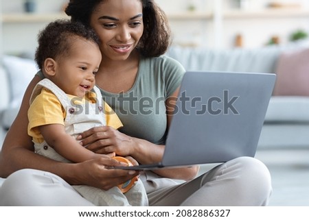 Smiling African American Mom And Her Cute Toddler Baby Relaxing With Laptop At Home, Mother And Child Watching Development Videos Or Cartoons While Sitting Together On Floor In Living Room, Closeup