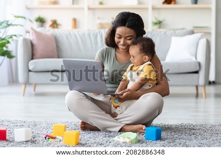 Black Young Mom Showing Development Videos On Laptop To Her Infant Baby At Home, Happy African American Mother Relaxing With Little Toddler Child On Floor In Living Room, Watching Cartoons Online