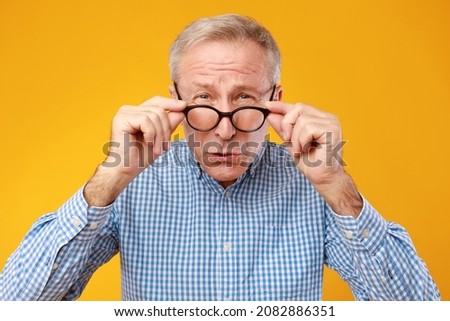 Poor Eyesight. Senior Man Can't See, Squinting Eyes Wearing Eyeglasses Having Problems With Vision, Looking At Camera, Yellow Orange Wall. Ophtalmic Issue In Older Age, Macular Degeneration Concept Royalty-Free Stock Photo #2082886351