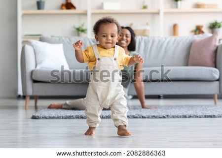 Baby Development. Cute Little Black Infant Boy Making First Steps At Home, Adorable African American Toddler Child Walking In Living Room, His Happy Mom Smiling On Background, Copy Space Royalty-Free Stock Photo #2082886363