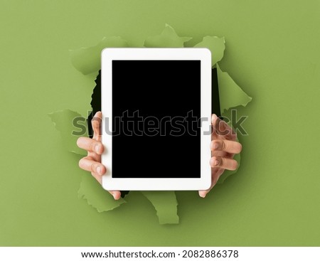 Website Ad Promo, Great Offer. Person holding tablet with black empty screen showing device breaking through green paper sheet hole. Vertical blank display with free copy space, mock up template