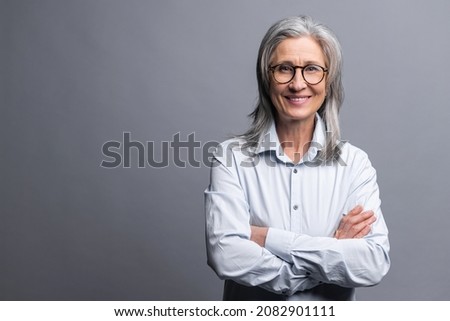 Successful senior mature gray-haired businesswoman with arms crossed isolated on gray, elder female entrepreneur ceo manager in glasses standing and confidently looking at the camera, hands folded Royalty-Free Stock Photo #2082901111
