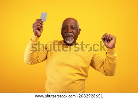 Elderly African American man showing credit card and making YES gesture on orange studio background. Happy senior black male using electronic money, celebrating big win or success Royalty-Free Stock Photo #2082928651