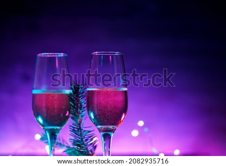 Two glasses of sparkling wine or champagne, neon Christmas background. Christmas Tree branch