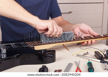Guitar master aligns the frets on guitar neck with leveling bar. Royalty-Free Stock Photo #2082940204