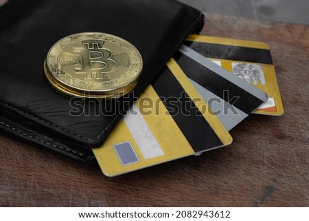 A black leather wallet with some bitcoins, coins and credit cards comin out from it. Economical emergency situation. Selective focus