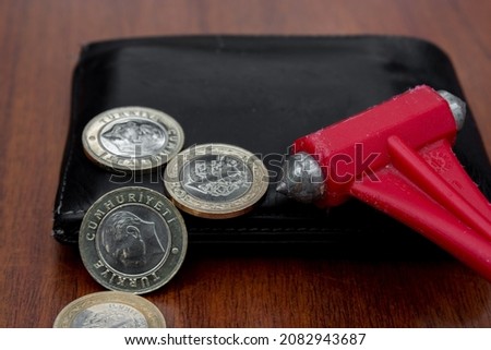 A black leather wallet with some bitcoin and a red emergency hammer hitting on it. Selective focus.