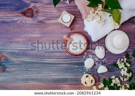 Flat lay spa composition with jasmine flowers, sea salt in bowl, towels on wooden background