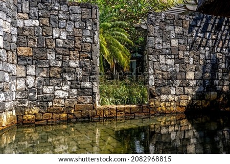 Old stone wall in the hotel with palm leaf in garden. Beautiful reflection in the water. Picture captured in the sunny morning. Mauritius island. High quality photo. 