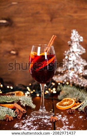 A glass of mulled wine on the wooden table surrounded by Christmas decorations. Festive winter drink vertical photo