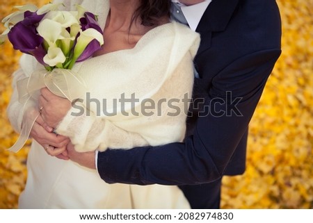 Man in suit hug female in cream sweater holding lily flower bouquet outdoors in autumn background
