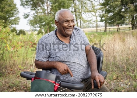 Portrait of a senior happy man living with HIV sitting on a bike designed for people with disability among the dry long grass
