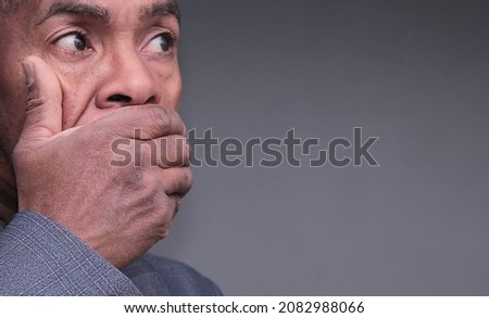man with hand over mouth not wanting to speak on grey background stock photo