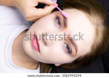 the face of a beautiful blonde model after the eyebrow lamination procedure, the master combs the eyebrows with a brush Royalty-Free Stock Photo #2082994294