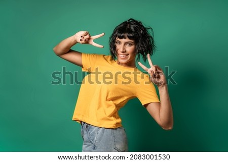 Joyful pretty brunette making the v, victory sign isolated on a green background - people concept of a cheerful successful young woman smiling and expressing satisfaction