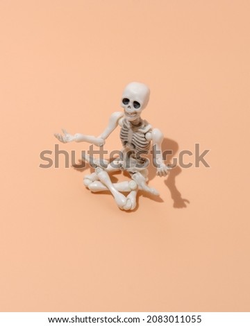 Plastic figurine of a skeleton sits in a lotus position on a beige background. The human skeleton is doing yoga, meditating.