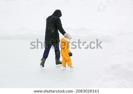 A father teaches a child to skate on the cleared ice of a frozen lake in the countryside. Dad leads his daughter by the hand, insuring her from falling. 
 Ice skating season on winter frosty days