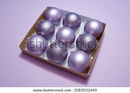 Cardboard box with collection of purple christmas balls. Concept of Xmas and New Year. Beautiful decorations for winter events, holidays and greetings. Isolated on purple background