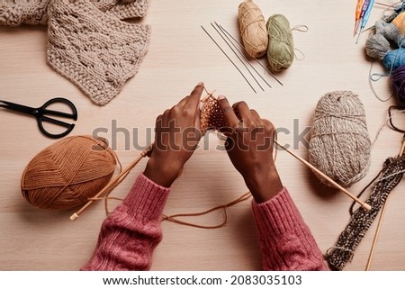 Top view of female hands knitting against wooden table in cozy light, copy space Royalty-Free Stock Photo #2083035103