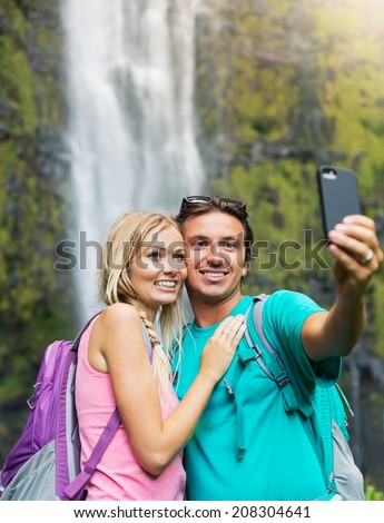 Couple having fun together outdoors. Taking self portrait with camera phone after hiking to incredible waterfall in Hawaii.