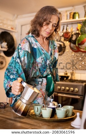 A vertical portrait shot of a healthy woman living with HIV pouring tea from a teapot in her kitchen in London