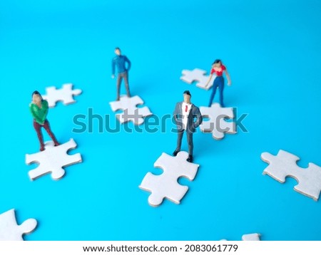 Miniature people and white jigsaw puzzle on a blue background.