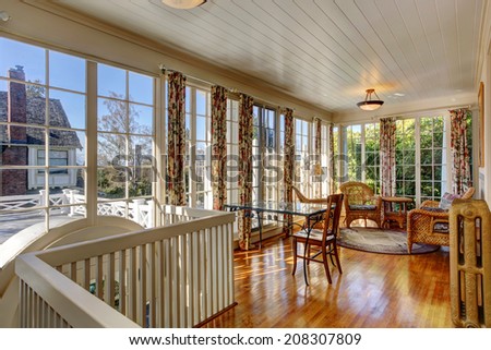 Bright sun room with french windows. Furnished with wicker table and chairs and glass top table