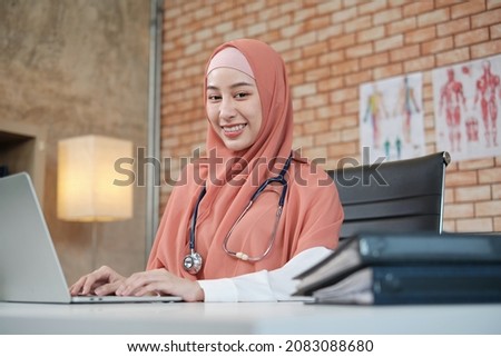 Portrait of a beautiful female doctor, beautiful Muslim in uniform with a stethoscope, smiling and working with laptop in hospital's clinic. One person who has expertise in professional treatment.