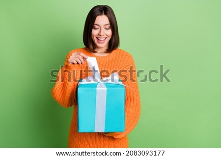 Portrait of attractive curious funny cheerful girl opening festal giftbox isolated over vibrant green color background