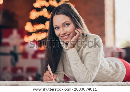 Photo of shiny charming lady wear knitted sweater smiling lying floor writing christmas congratulations indoors house home room