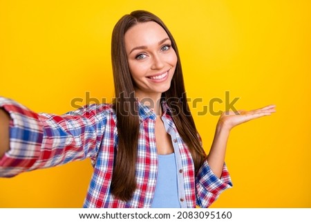 Photo of cheerful lady make selfie palm hold empty space novelty wear plaid shirt isolated yellow color background