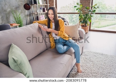Photo of adorable pretty young lady dressed yellow shirt typing modern gadget smiling indoors room home house