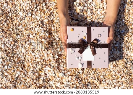 Hands hold out a gift against the background of the beach of small shells. Top view.