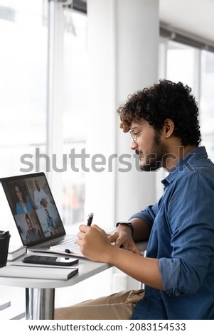 Focused young indian man listening interracial speakers watching lecture seminar webinar online and writing notes looking at laptop screen. Studying remotely or distant interview side view
