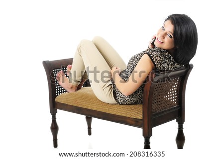 A beautiful teen girl reclined on a bench, happily looking back at the viewer while chatting on her phone.  On a white background.