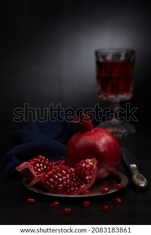Still life with pomegranate, middle aged styled glass with vine, knife, napkin and silver dish on a dark stone table and dark background. vertical photo with shallow depth of field.  