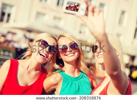 holidays and tourism, modern technology concept - beautiful girls taking picture with digital camera in the city