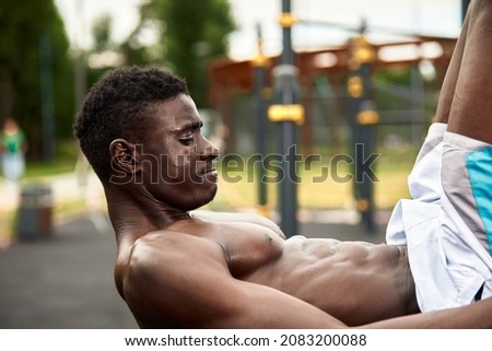 Young black man doing crunches outdoors. He is in a park.