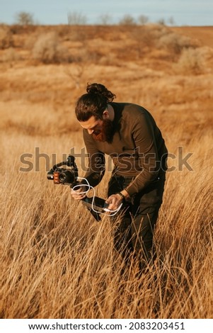 Photo of bearded man filming with camera and gimbal on fields at sunset