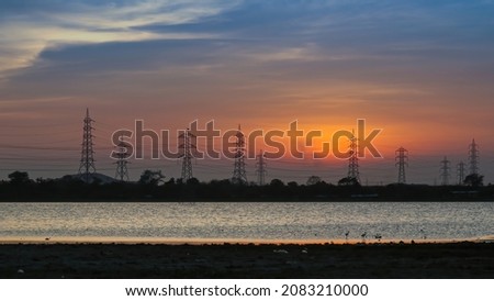 A lake beach during sunset surrounded by city pollutions mobile signal tower with beautiful clouds