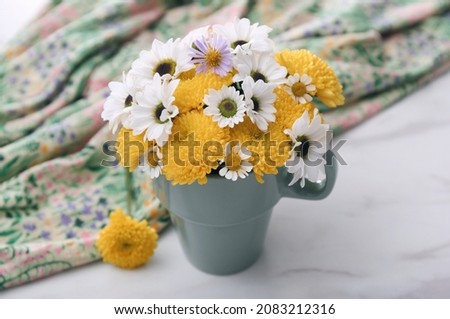 Beautiful bright flowers in cup and fabric on white marble table, closeup
